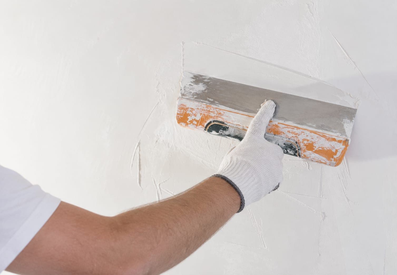 Close-up van een hand met spaan die een wand glad plamuurt